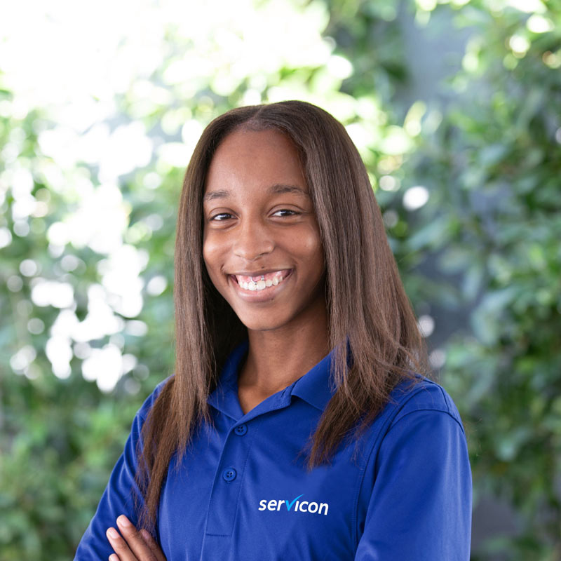 A servicon employee, Tatianna, stands in front of greenery